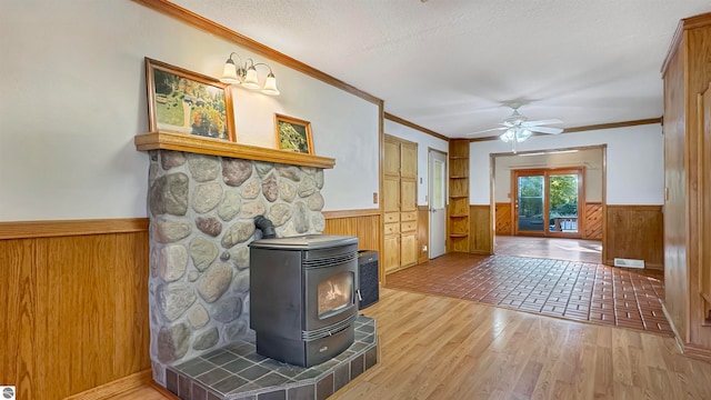 living room with hardwood / wood-style flooring, a wood stove, crown molding, a textured ceiling, and ceiling fan