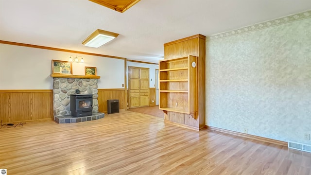 unfurnished living room with wood walls, ornamental molding, light hardwood / wood-style floors, and a wood stove