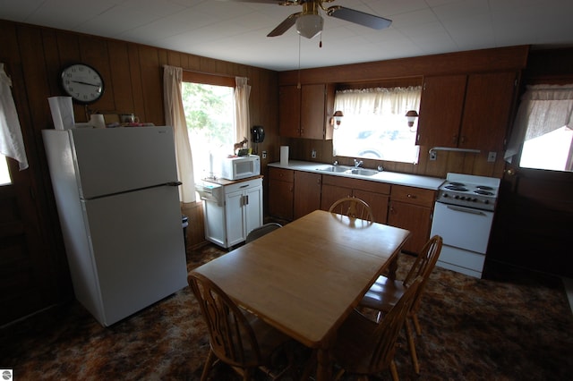 kitchen featuring white appliances, ceiling fan, wood walls, and sink