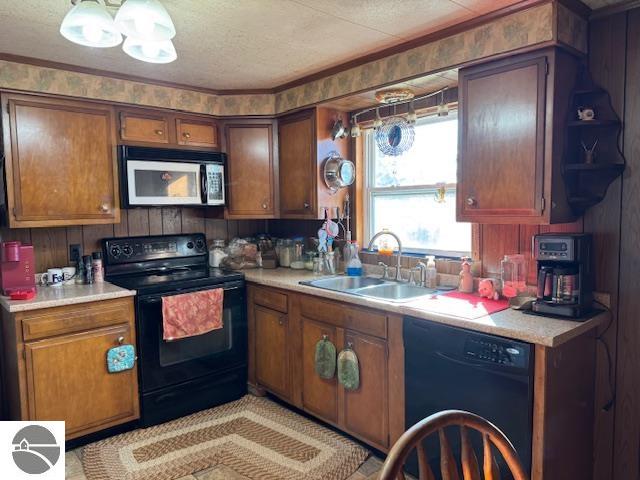 kitchen with a textured ceiling, black appliances, sink, and wood walls