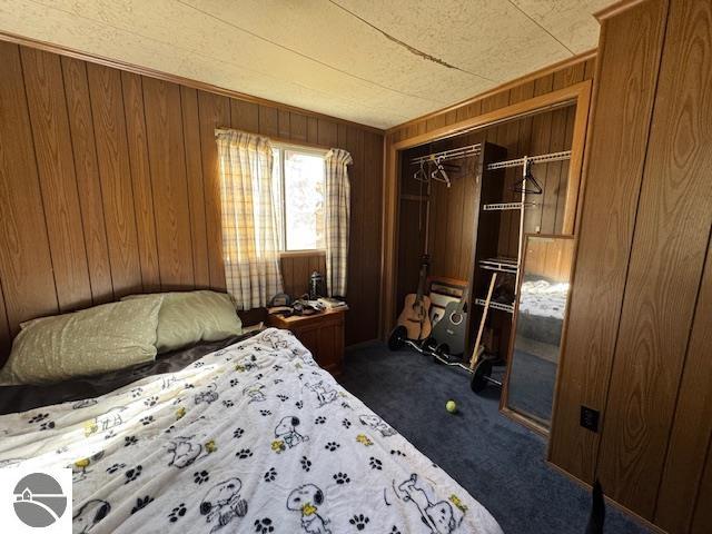 bedroom featuring a closet, wooden walls, and dark carpet