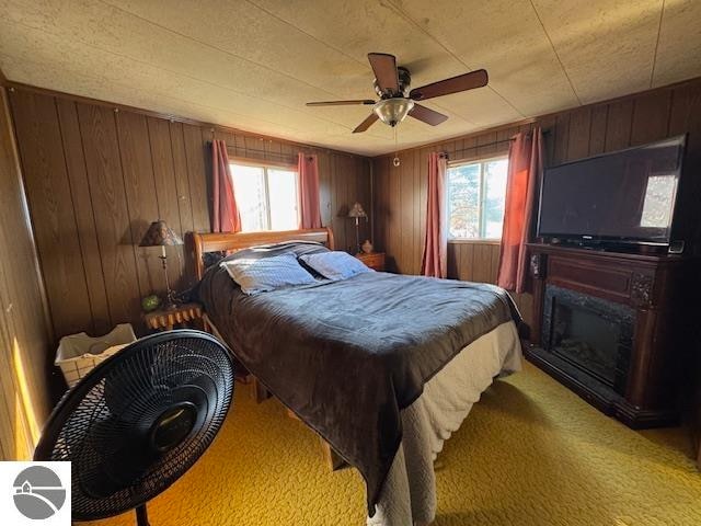 bedroom featuring ceiling fan, wood walls, and light carpet