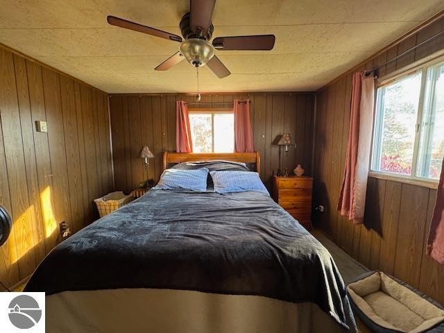 bedroom with wooden walls, multiple windows, and ceiling fan