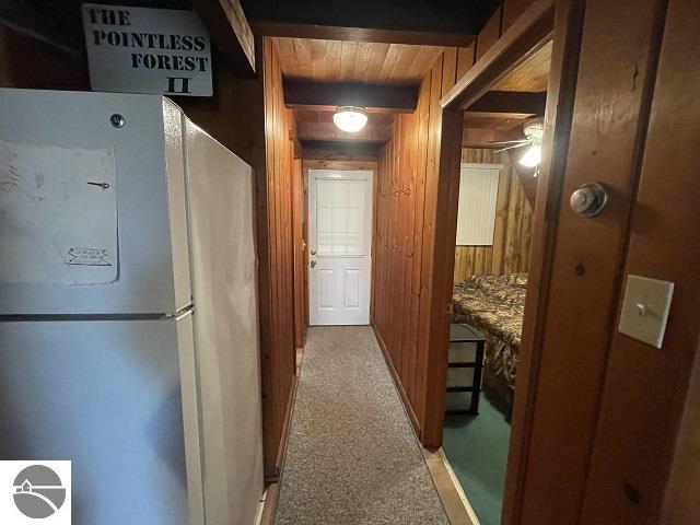 hallway with carpet, wood ceiling, wood walls, and beamed ceiling