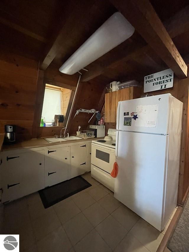 kitchen with white cabinetry, beamed ceiling, sink, wooden walls, and white appliances