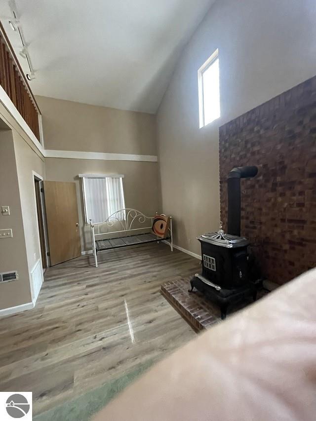 bonus room featuring light hardwood / wood-style floors, high vaulted ceiling, and a wood stove