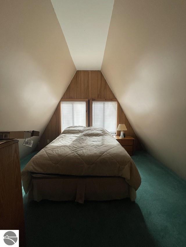 carpeted bedroom with wood walls and vaulted ceiling