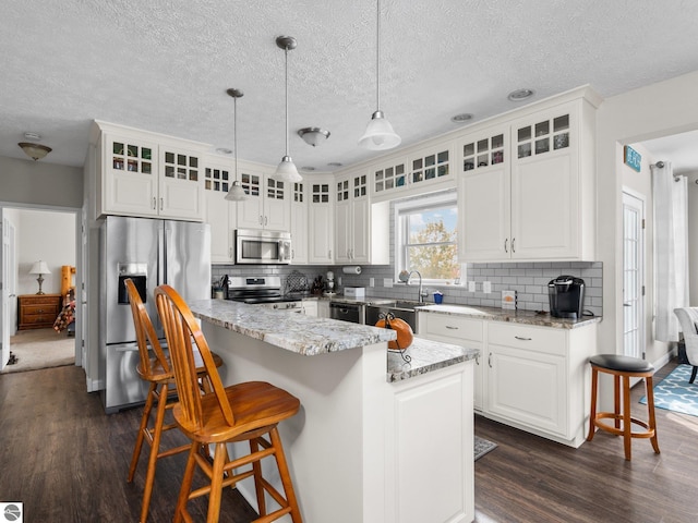 kitchen featuring a kitchen island, appliances with stainless steel finishes, decorative light fixtures, and dark hardwood / wood-style flooring