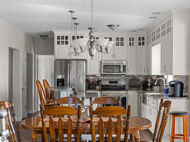 kitchen featuring backsplash, stainless steel appliances, decorative light fixtures, white cabinets, and light stone counters