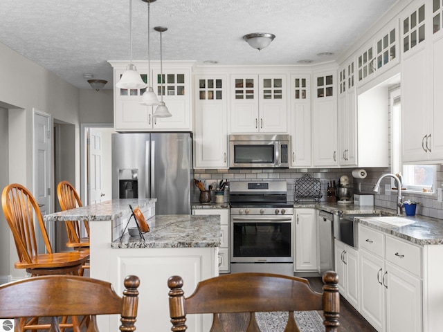 kitchen featuring a center island, stainless steel appliances, decorative light fixtures, white cabinets, and light stone counters