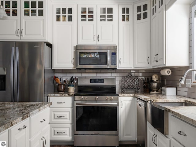 kitchen featuring appliances with stainless steel finishes, white cabinetry, light stone counters, and backsplash