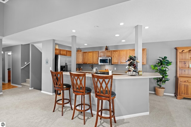 kitchen with a center island with sink, a kitchen bar, stainless steel appliances, and light colored carpet