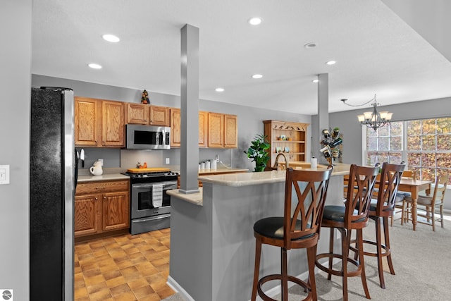 kitchen with appliances with stainless steel finishes, a kitchen breakfast bar, hanging light fixtures, an inviting chandelier, and a kitchen island with sink