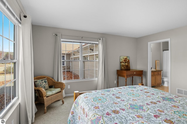 bedroom with connected bathroom, multiple windows, and light colored carpet