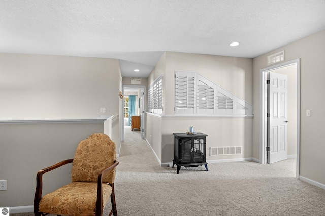 living area with a wood stove, a textured ceiling, and light colored carpet