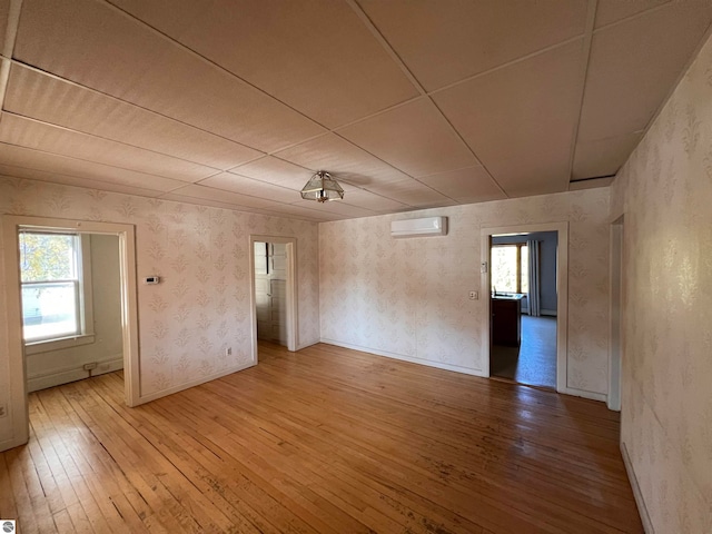 unfurnished room featuring a healthy amount of sunlight, a wall mounted air conditioner, and hardwood / wood-style floors