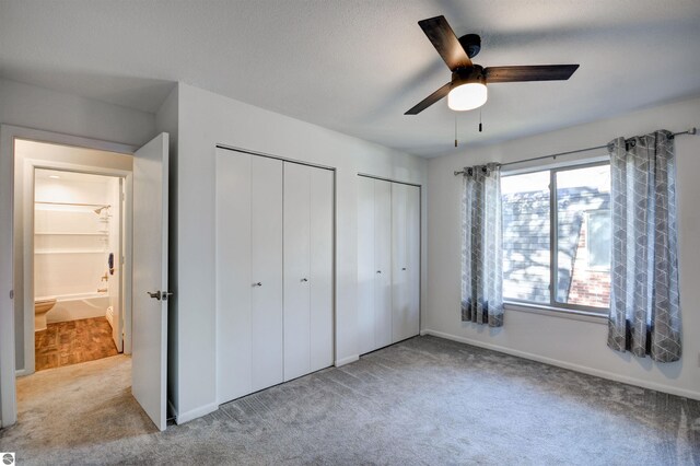 unfurnished bedroom with light carpet, two closets, and ceiling fan