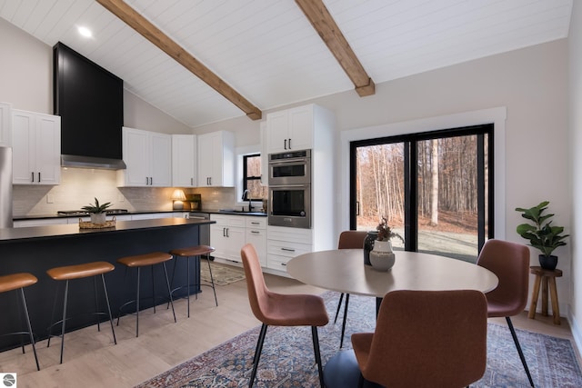 dining space with light hardwood / wood-style flooring, beamed ceiling, high vaulted ceiling, and sink