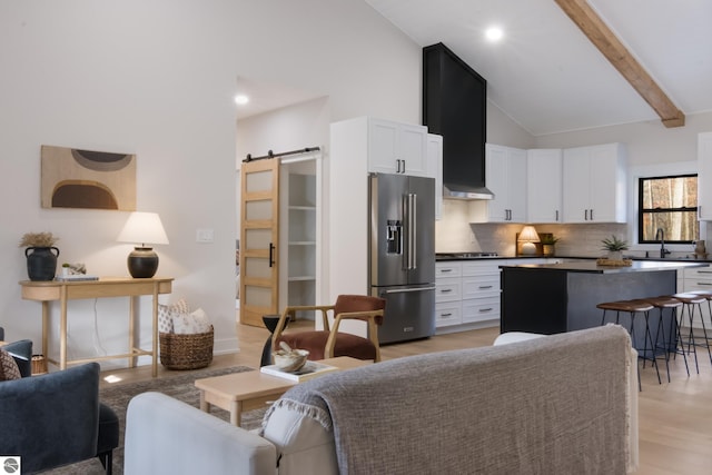 living room with sink, a barn door, beamed ceiling, high vaulted ceiling, and light hardwood / wood-style floors