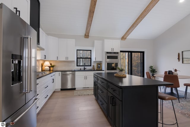 kitchen featuring light wood-type flooring, a kitchen island, a kitchen bar, white cabinetry, and stainless steel appliances