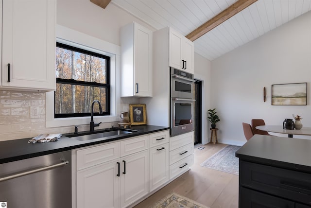 kitchen with white cabinetry, sink, stainless steel appliances, lofted ceiling with beams, and light hardwood / wood-style floors