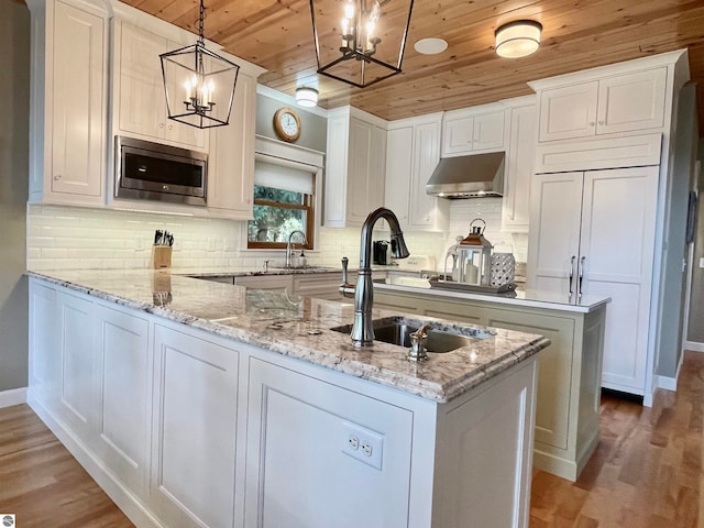 kitchen featuring wood ceiling, stainless steel microwave, range hood, pendant lighting, and white cabinets