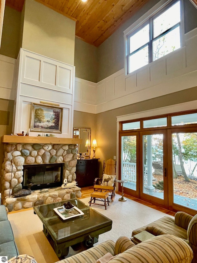 carpeted living room featuring a wealth of natural light, a stone fireplace, high vaulted ceiling, and wooden ceiling