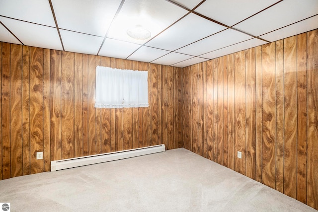 unfurnished room with a paneled ceiling, wood walls, carpet, and baseboard heating