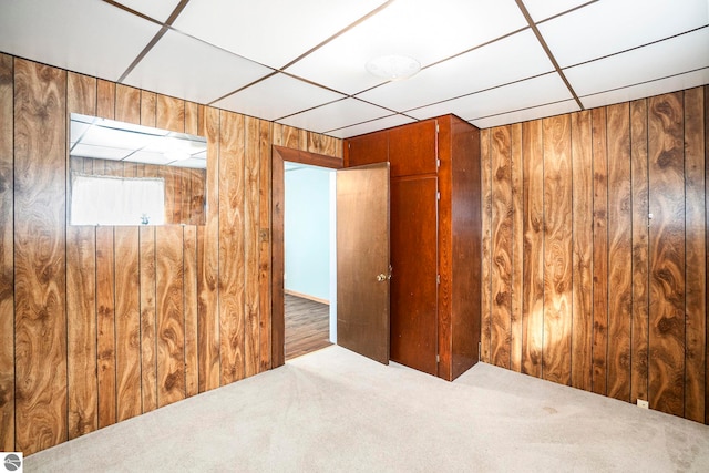 carpeted empty room with wood walls and a drop ceiling