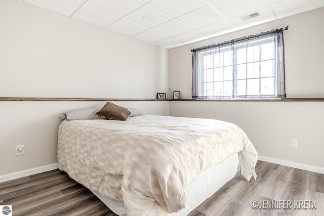 bedroom featuring wood-type flooring and a drop ceiling