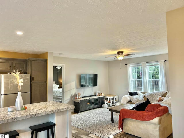 living room featuring light hardwood / wood-style flooring, a textured ceiling, and ceiling fan