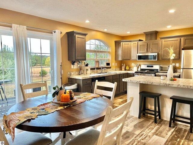 kitchen with sink, stainless steel appliances, light stone countertops, and light hardwood / wood-style flooring