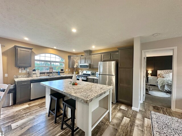 kitchen featuring sink, a kitchen island, a textured ceiling, stainless steel appliances, and dark hardwood / wood-style floors