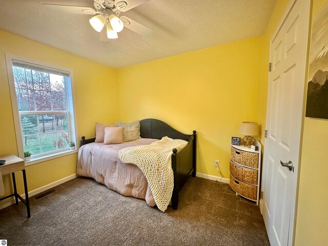 bedroom featuring ceiling fan, a textured ceiling, and dark carpet