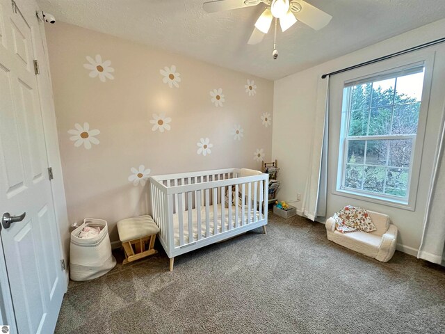 bedroom with carpet, a textured ceiling, a crib, and ceiling fan