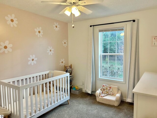 carpeted bedroom featuring a textured ceiling, a crib, and ceiling fan