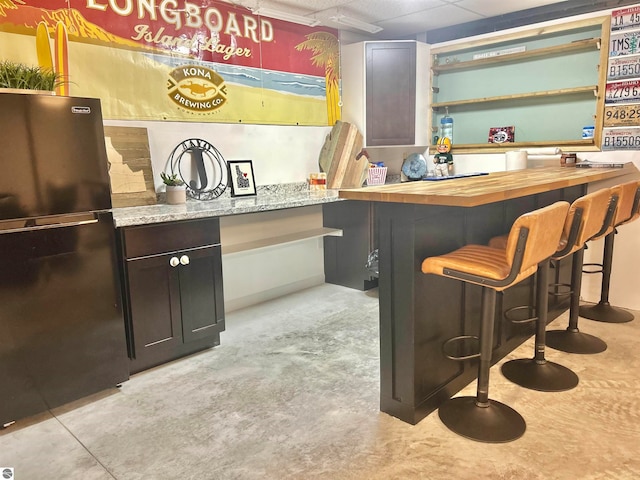 bar with wood counters, dark brown cabinetry, and black refrigerator