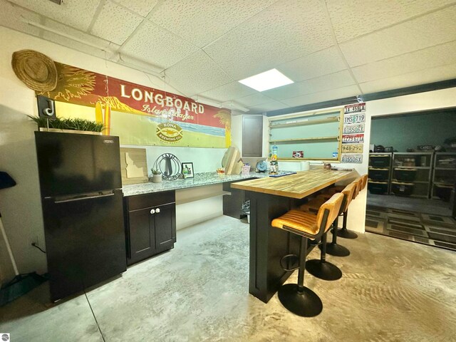 kitchen featuring butcher block countertops, a drop ceiling, and black fridge