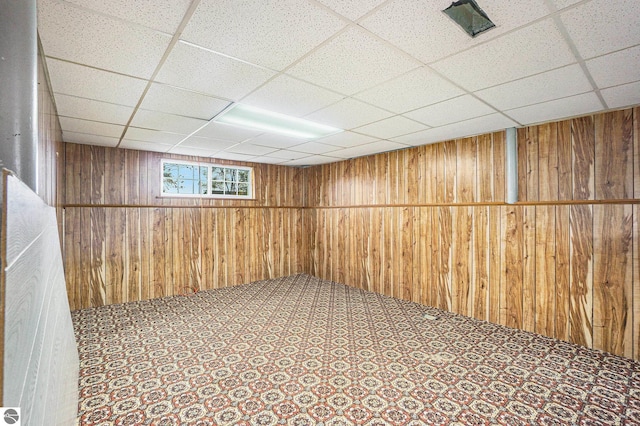 basement featuring a drop ceiling and wooden walls