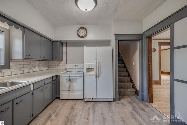 kitchen featuring white appliances, a sink, light wood-style floors, gray cabinets, and decorative backsplash