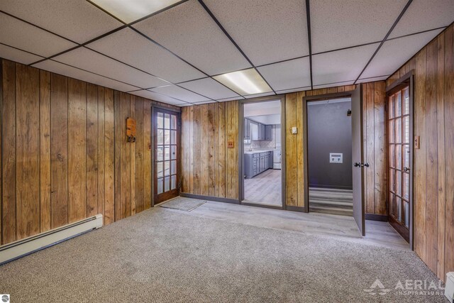 empty room with wooden walls, a paneled ceiling, a baseboard heating unit, carpet flooring, and independent washer and dryer