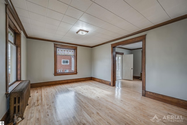 spare room featuring baseboards, crown molding, light wood finished floors, and radiator heating unit