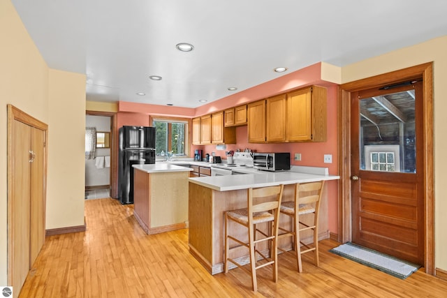 kitchen featuring kitchen peninsula, black fridge, light hardwood / wood-style floors, white electric range oven, and a breakfast bar