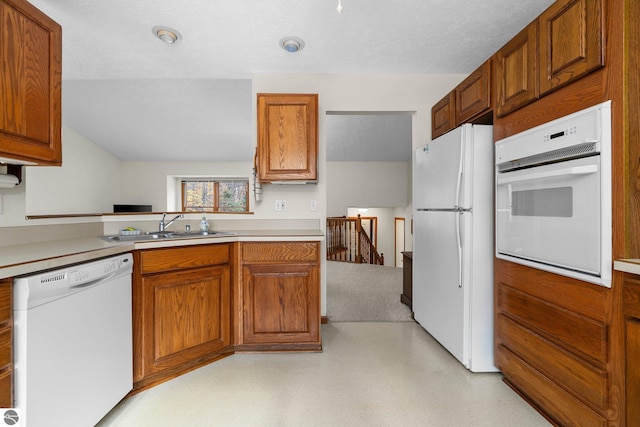 kitchen featuring a textured ceiling, kitchen peninsula, white appliances, and sink