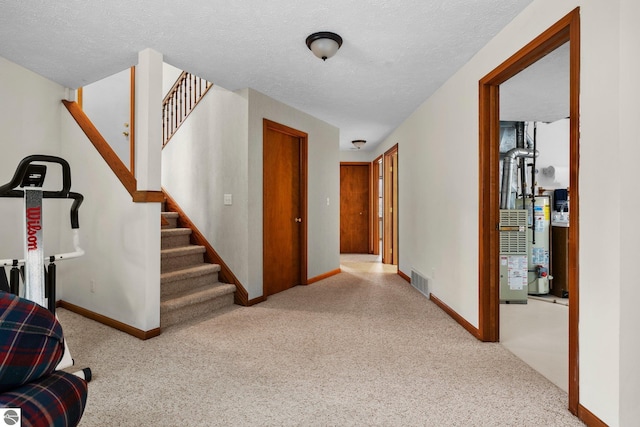 hall featuring a textured ceiling, light colored carpet, and gas water heater