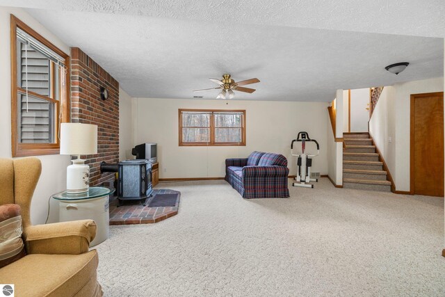 living room featuring carpet, a textured ceiling, a wood stove, and ceiling fan