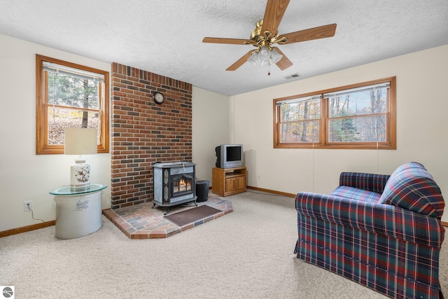 living room with a wood stove, ceiling fan, carpet, and a textured ceiling