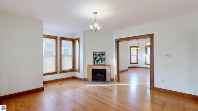 unfurnished living room with an inviting chandelier, light hardwood / wood-style flooring, and a brick fireplace