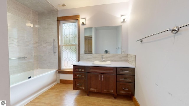 bathroom with vanity, hardwood / wood-style floors, tiled shower / bath combo, and backsplash