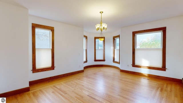 spare room with hardwood / wood-style flooring and an inviting chandelier